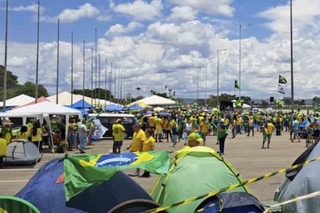 Apoiadores do presidente derrotado nas eleições Jair Bolsonaro com camisas amarelas e barracas com bandeiras do Brasil no QG do Exército, em Brasília. O céu está azul e com nuvens - Metrópoles