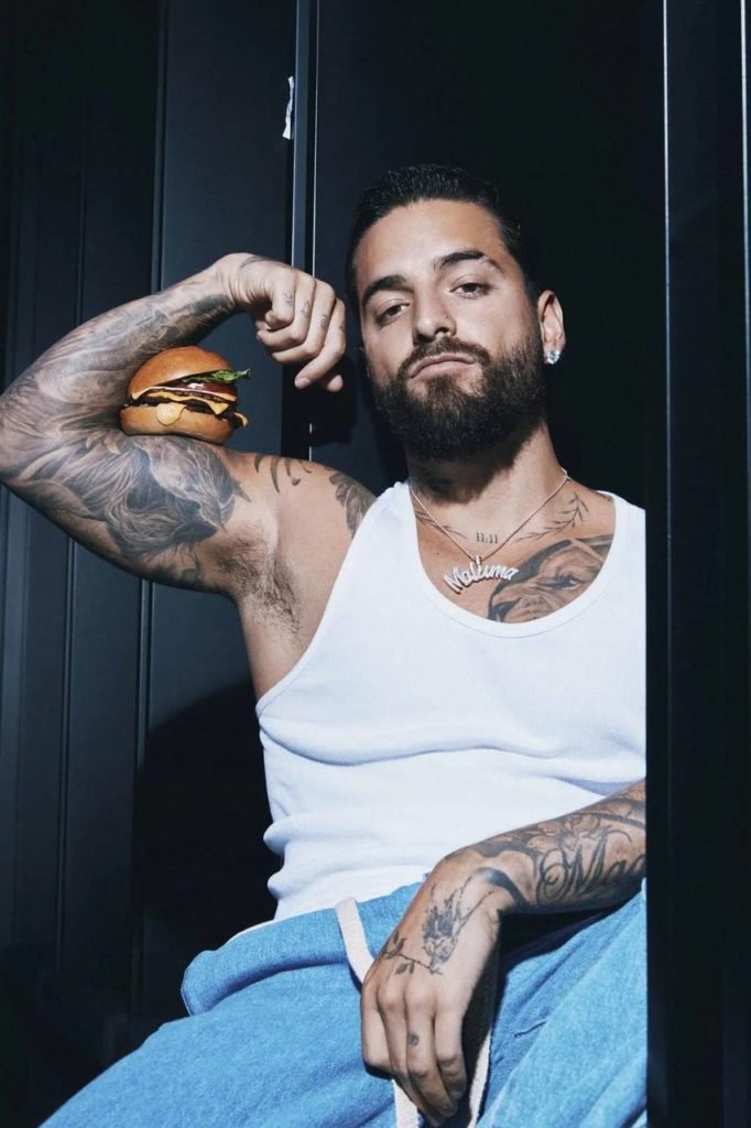 Na foto, o cantor Maluma posa para a câmera com um hambúrguer no braço - Metrópoles