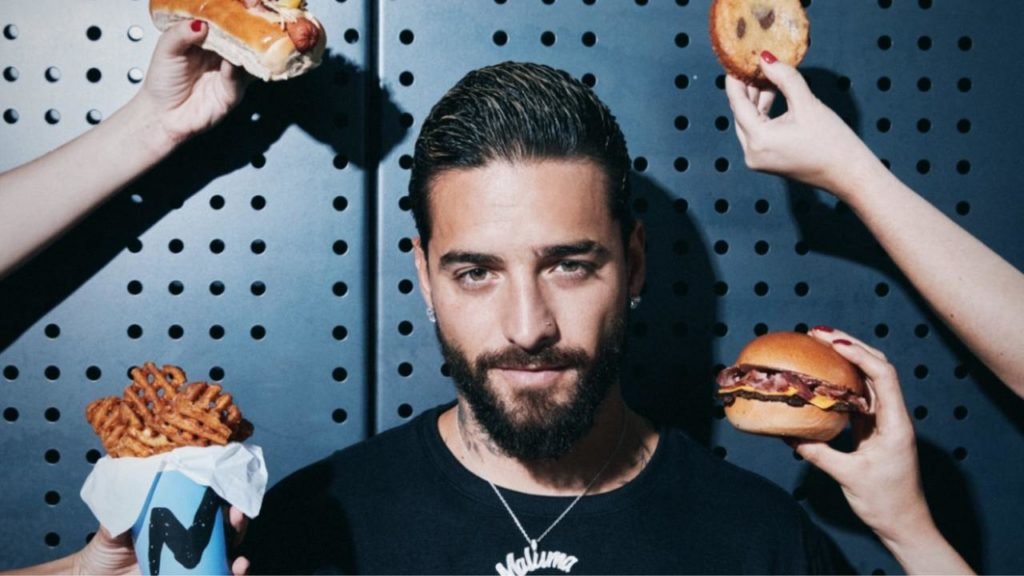 Na foto, o cantor Maluma posa para a câmera rodeado de comidas de fast-food - Metrópoles