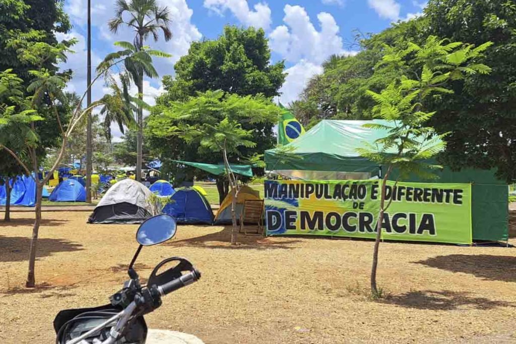 Apoiadores do presidente derrotado nas eleições Jair Bolsonaro com camisas amarelas e barracas com bandeiras do Brasil no QG do Exército, em Brasília. O céu está azul e com nuvens - Metrópoles