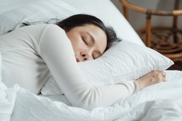 Mulher asiática dormindo em cama - Metrópoles