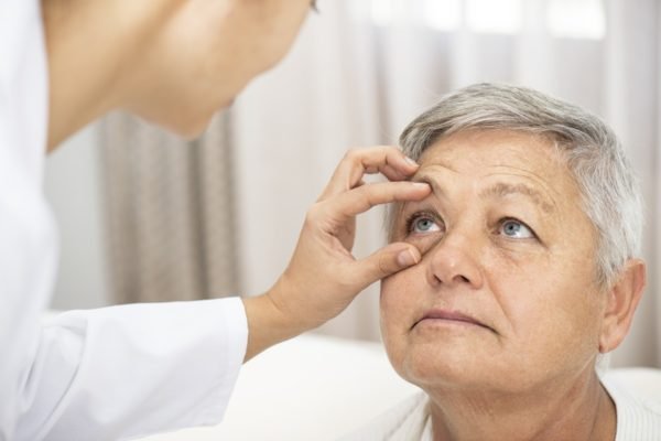 Foto de uma mulher com olho aberto sendo examinada por uma médica