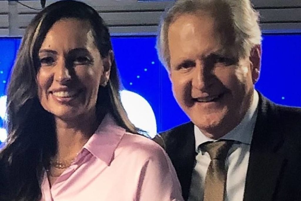 mulher vestida de camisa rosa sorri ao lado de homem de cabelos brancos que veste terno e sorri - Metrópoles