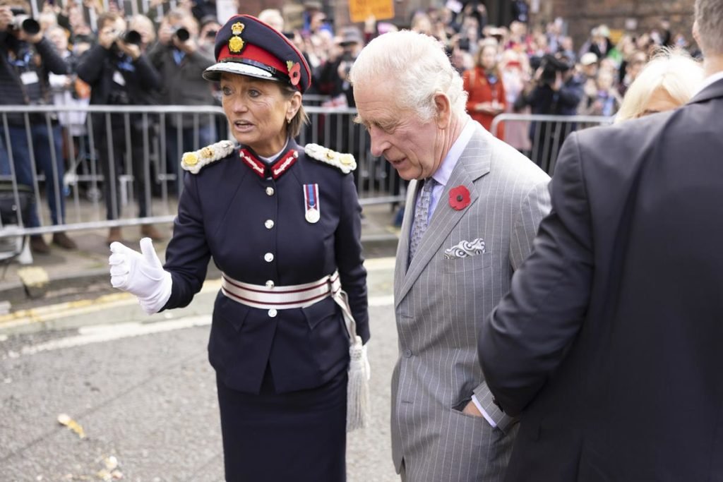 Foto colorida de mulher vestida com trajes militares ao lado de homem com terno cinza