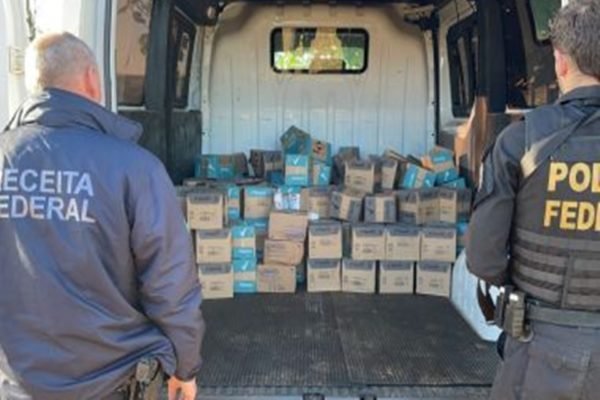 Dois agentes da Polícia Federal (PF) em pé em cima de uma van cheia de caixas de vinho