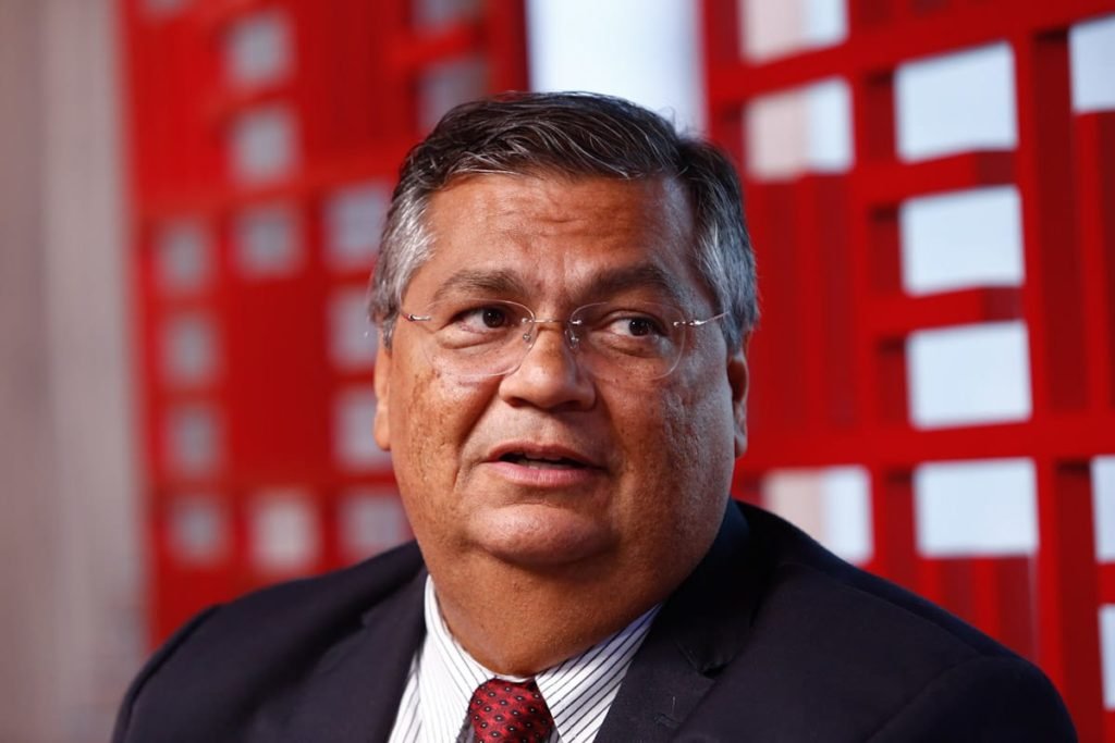 Senador eleito pelo Maranhão, Flávio Dino, dá entrevista ao Metrópoles. Ele olha para o lado frente a fundo vermelho - Metrópoles