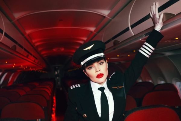 Foto colorida da Gkay. Ela está no interior de um avião com luzes vermelhas, vestida de aeromoça - Metrópoles