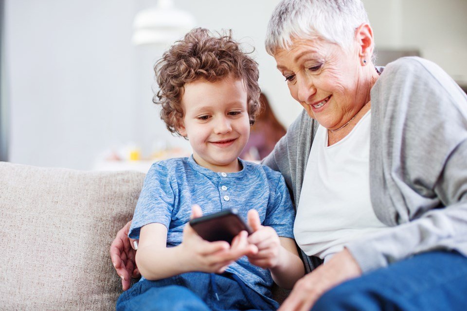 Foto colorida de menino segurando um celular ao lado de uma mulher branca idosa - Metrópoles