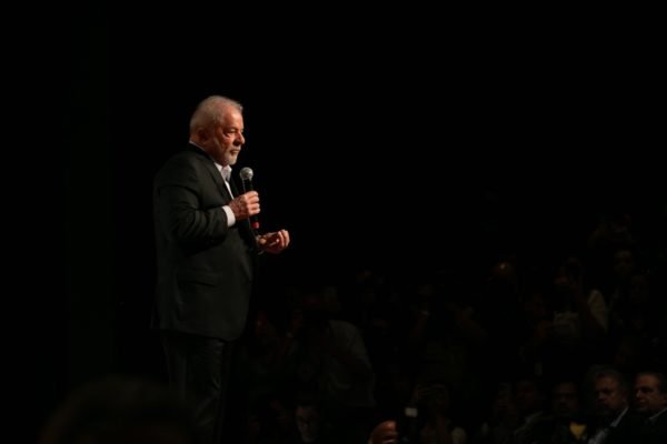 Imagem colorida mostra Luiz In&aacute;cio Lula da Silva, presidente eleito, em p&eacute; em um palco. Ele usa terno e segura um microfone - Metr&oacute;poles