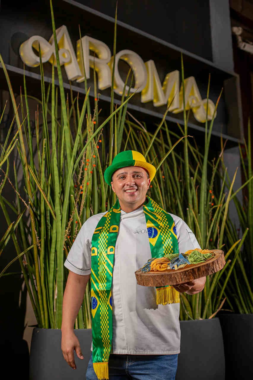 Na foto, o Chef Ronny Peterson com vestes de Copa do Mundo segurando uma bandeja com comidas - Metrópoles