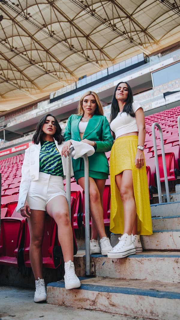Na imagem com cor, 3 mulheres posam em estádio de futebol com cores da bandeira do país - Metrópoles