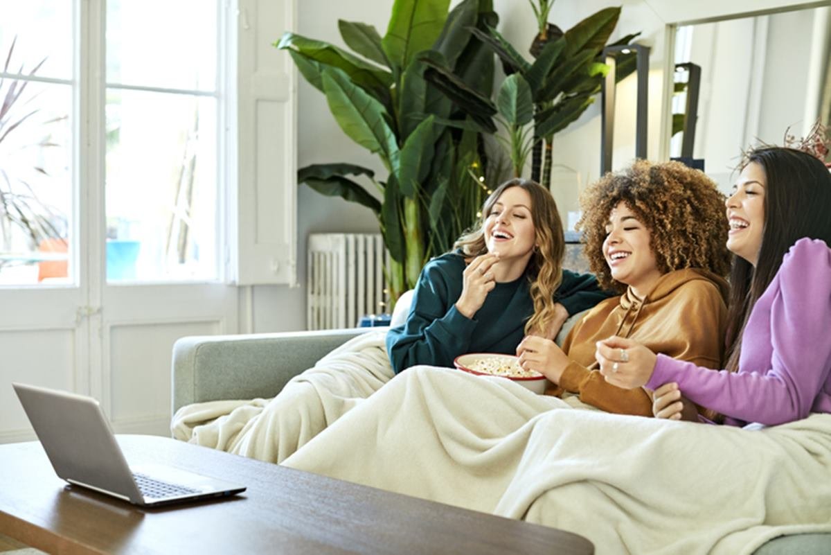 Três mulheres sentadas no sofá assistindo filme no computador - Metrópoles