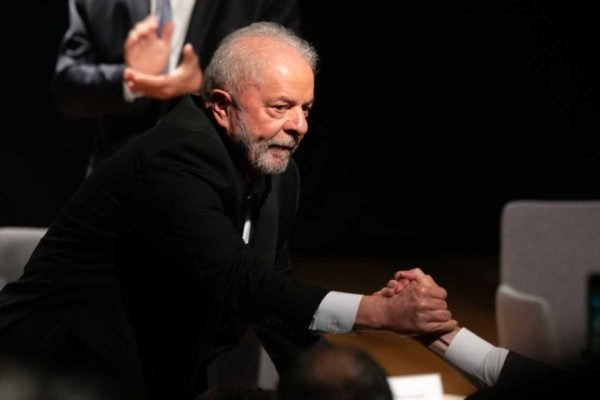 O presidente eleito Lula cumprimenta aliado, segurando sua mão, no palco do CCBB, sede do governo de transição - Metrópoles