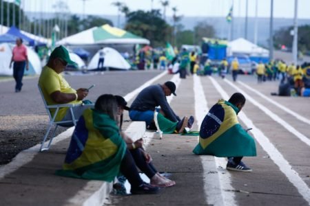Manifestantes sentados enrolados na bandeira do Brasil