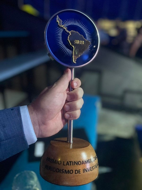 Imagem colorida com uma mão que segura Troféu do Prêmio Latino-americano de Jornalismo de Investigação - Metrópoles