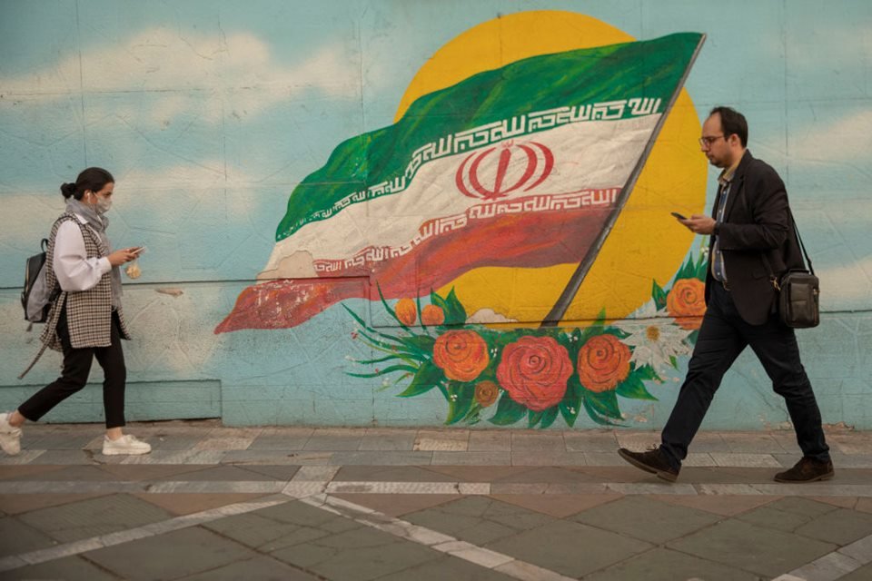 Em imagem colorida, Uma mulher iraniana caminha pelas ruas de Teerã, no Irã sem um lenço obrigatório. No sentido contrário, caminha um homem - Metrópoles