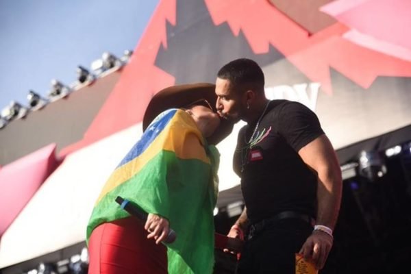 Cantora Maraisa de vestido vermelho e chapéu, com uma bandeira do Brasil enrolada ao corpo beijando o ex-BBB Bil Araújo em cima do palco - Metrópoles