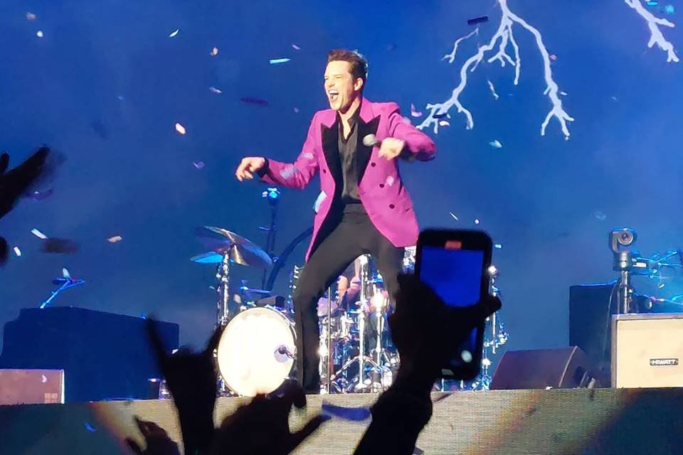 Cantor Brandon Flowers de blazer rosa no palco cantando - Metrópoles