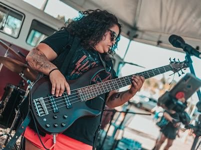 Mulher morena e de cabelo cacheado tocando baixo