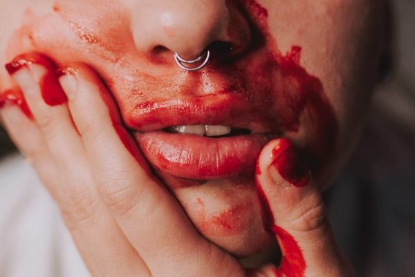 Close de mulher suja de sangue com a mão na boca - Metrópoles