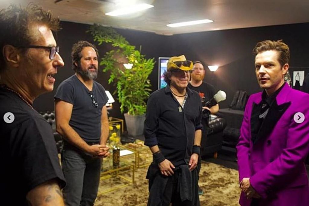 Dinho Ouro Preto a um canto conversando com Brandon Flowers, que está em outro canto, e dois homens entre eles - Metrópoles