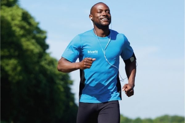 Homem negro está correndo sorridente com uma camisa azul da Bluefit - Metrópoles