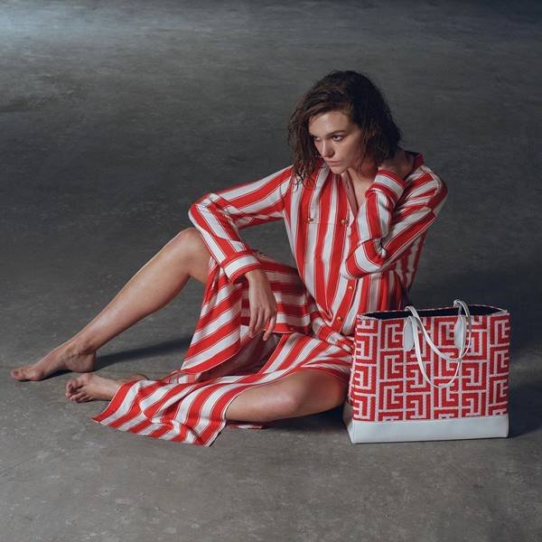 Mulher sentada no chão com roupa listrada branco e vermelho e bolsa com as mesma estampa ao lado - Metrópoles 