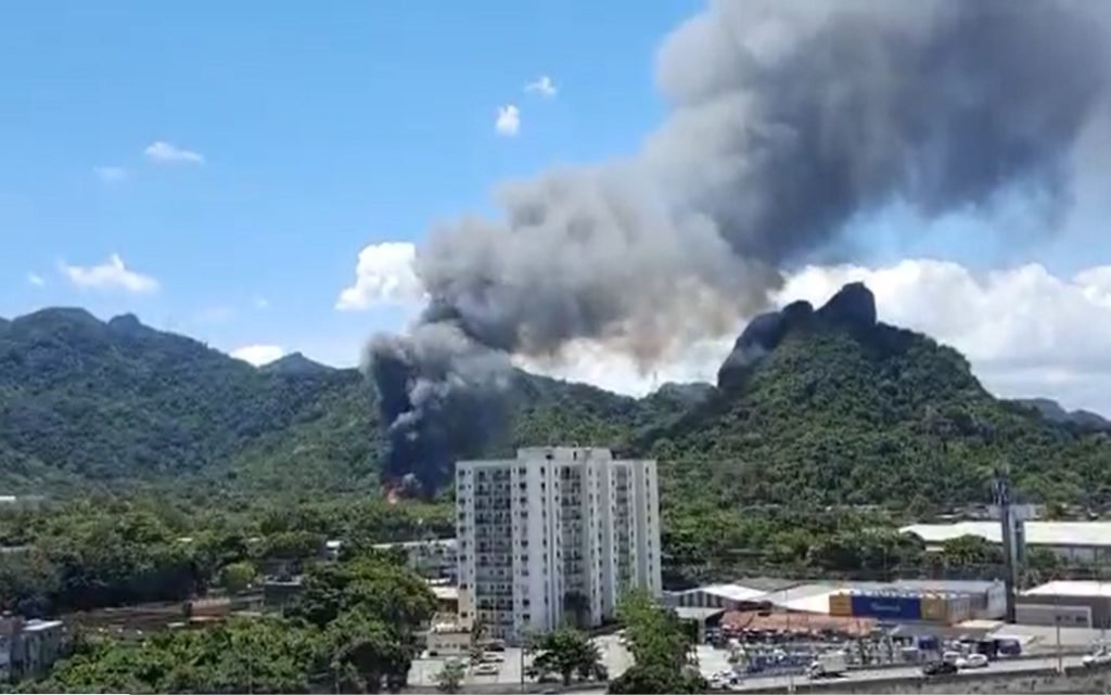 Incêndio atinge Projac, da Globo, no Rio de Janeiro. É possível ver muita fumaça saindo do meio de uma mata em morro, próximo a prédios - Metrópoles