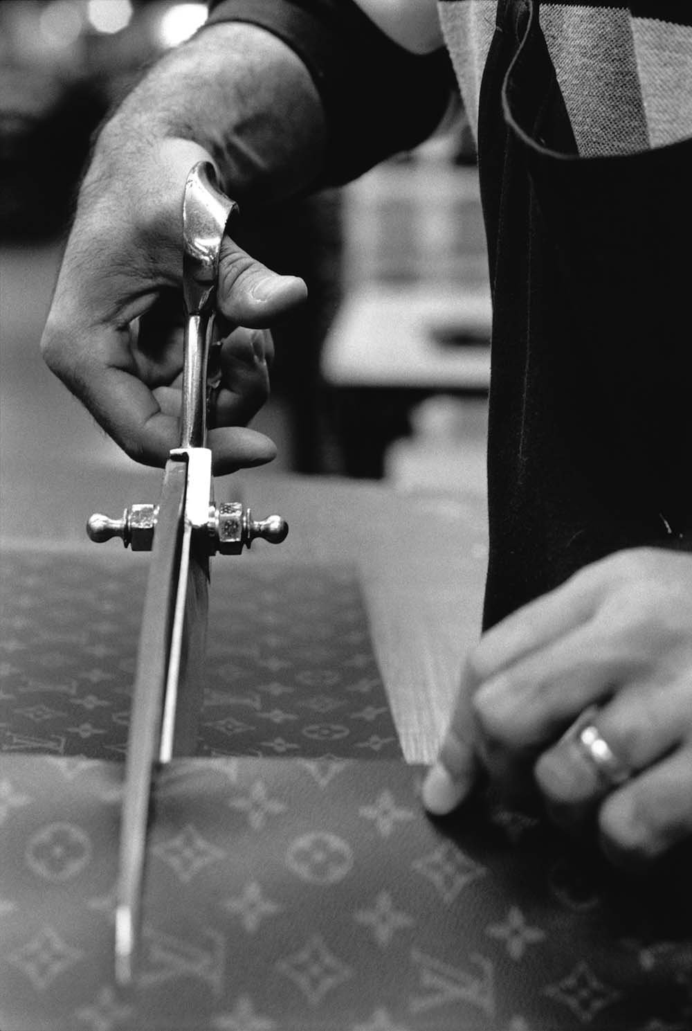 Fase de produção de uma bolsa "élipse" em canvas Monogram nas oficinas da Louis Vuitton em 4 de fevereiro de 1999 em Asnières, França. Na foto é posível ver as mãos de uma pessoa com uma tesoura grande e própria para couro cortando otecido.