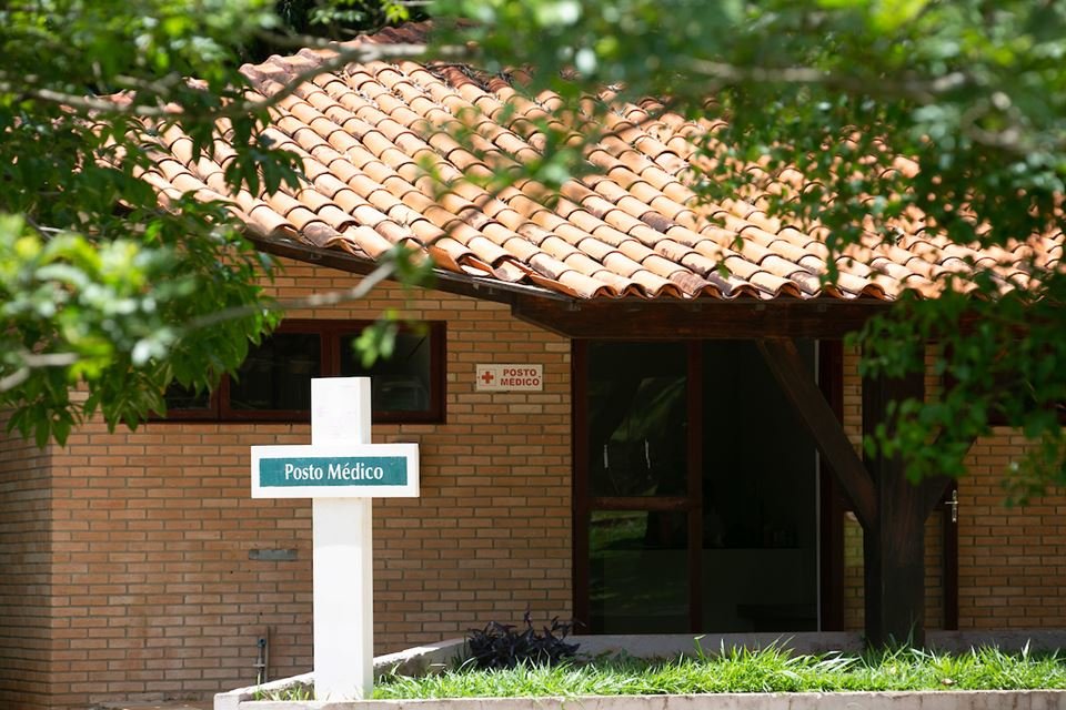 Casa com telhado de tijolos, árvore em cima e placa no formato de cruz à frente