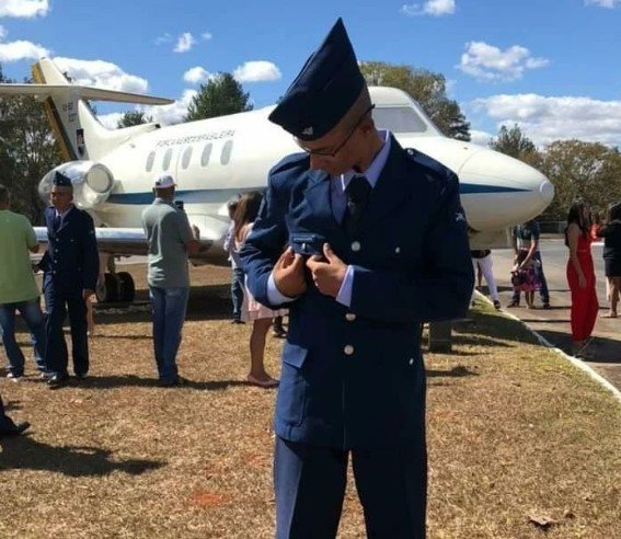 Homem com terno, óculos e chapéu de militar da FAB em frente ao avião