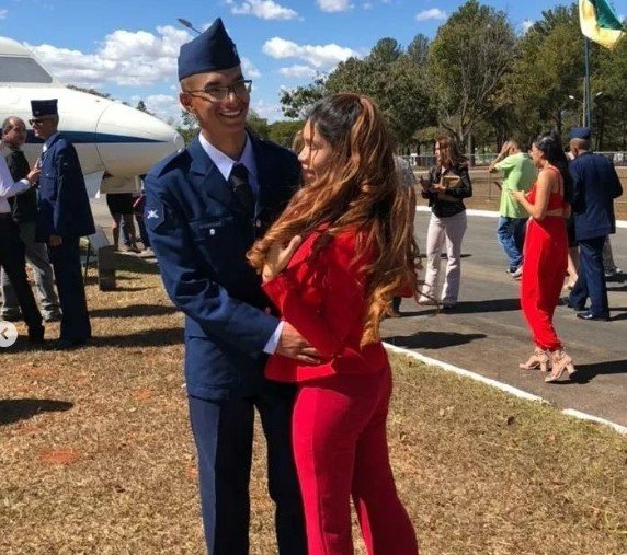 Menino com terno e chapéu azul abraçando menina com roupa vermelha