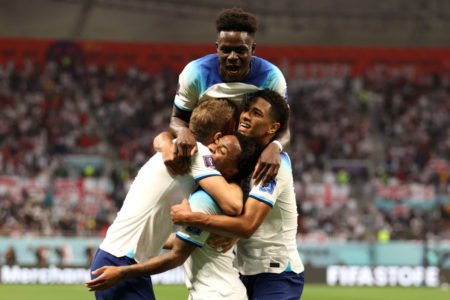 Jogadores da Inglaterra comemoram gols em sua estreia na Copa do Mundo. Ele se abraçam no campo e ao fundo, vê-se a arquibancada cheia - Metrópoles