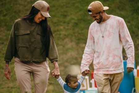 A cantora trans Pepita em foto com seu marido. Ambos sorriem e olham pro filho pequeno, de mãos dadas com ele - Metrópoles