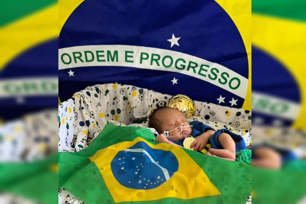 Foto de um bebê com a bandeira ordem e progresso ao fundo