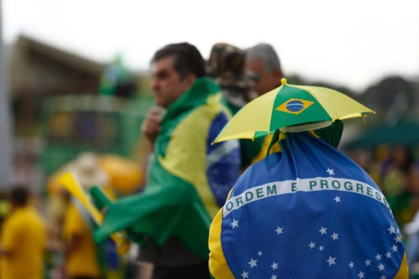 foto colorida de bolsonaristas com bandeira do Brasil e camisa da Seleção no qg do exército