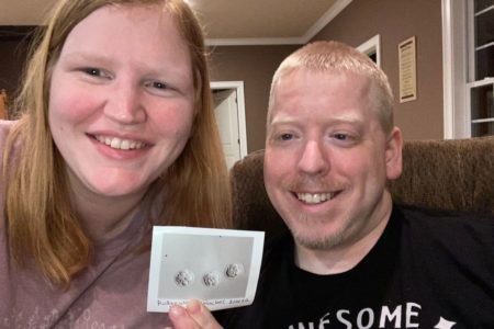 foto colorida de casal feliz segurando imagem de três embriões