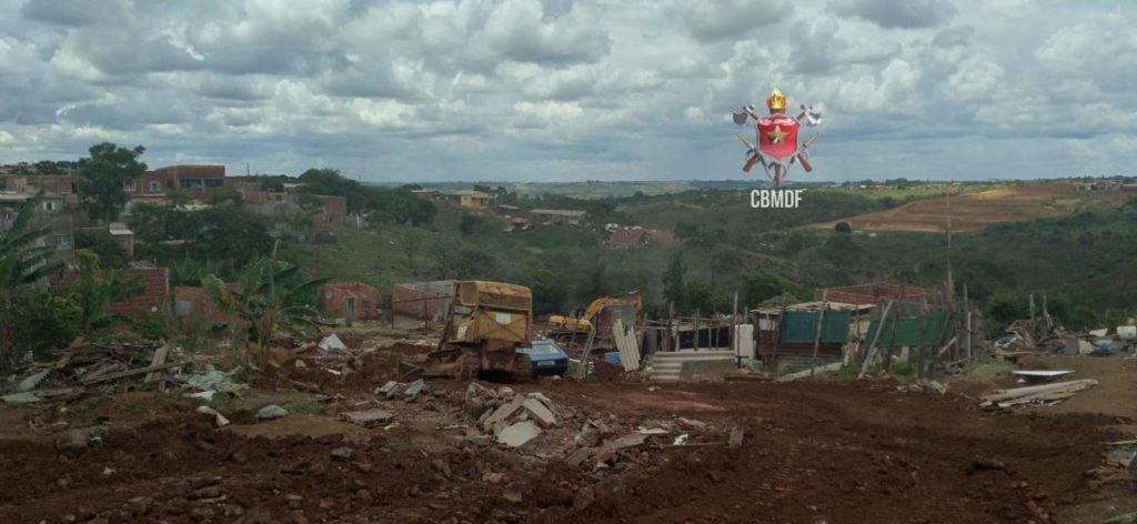Escavadeira manobra em área afetada pela chuva em Sol Nascente. Chão de terra. Foto colorida