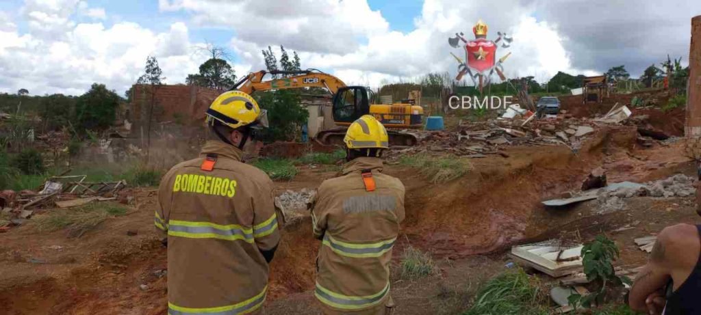 Bombeiros militares em uniforme pardo observam área devastada pela chuva em Sol Nascente.Chão de terra. Foto colorida