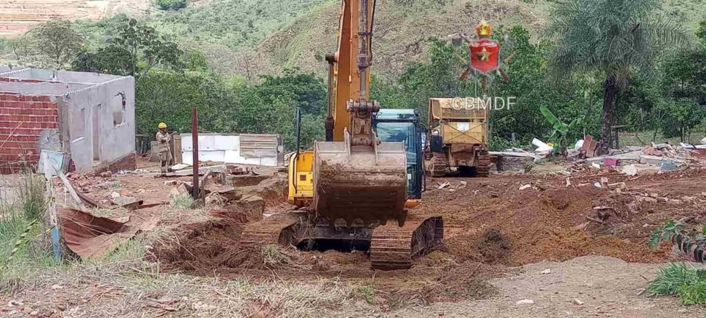 Escavadeira manobra em área afetada pela chuva em Sol Nascente. Chão de terra. Foto colorida