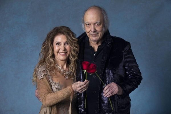 Wanderléa e Erasmo Carlos posam abraçados sorrindo e segurando uma rosa vermelha cada - metrópoles
