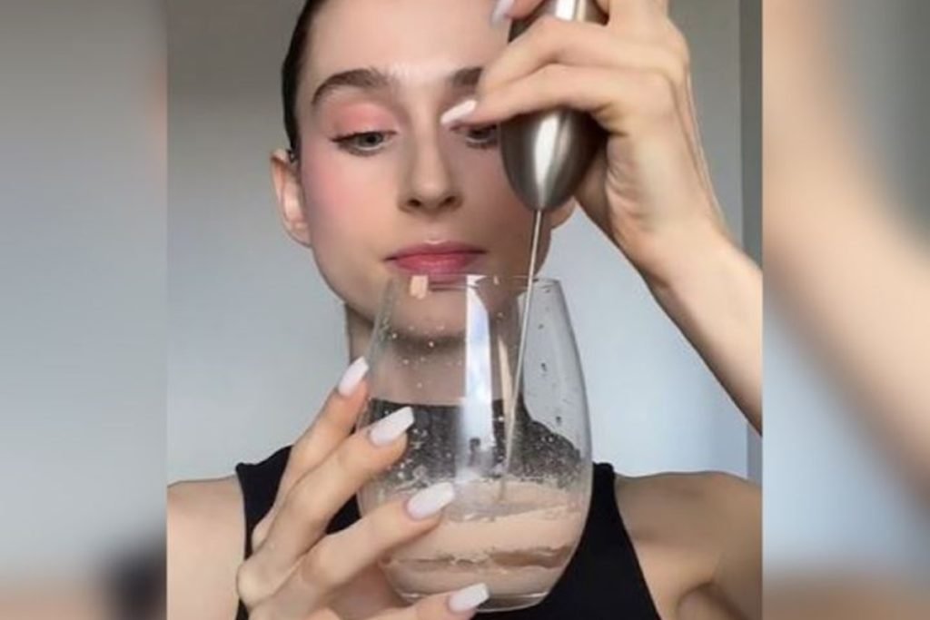 Foto colorida de mulher misturando base com água em um copo com um mixer-Metrópoles