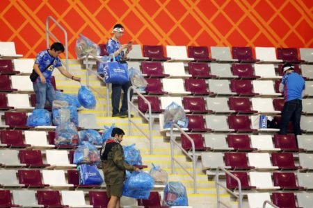 Torcida do Japão limpa estádio após vitória contra Alemanha. Na imagem, eles coltema lixo dentro de sacolas azuis em arquibancadas - Metrópoles