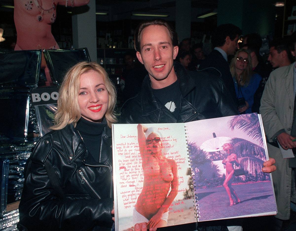 Um mulher e um homem, ambos jovens e brancos, seguram o livro Sex da cantora Madonna. A fotografia mostra Madonna nua, com os seis à mostra, e de óculos escuro. A foto foi feita em 1992, ano de publicação e de proibição do livro. - Metrópoles