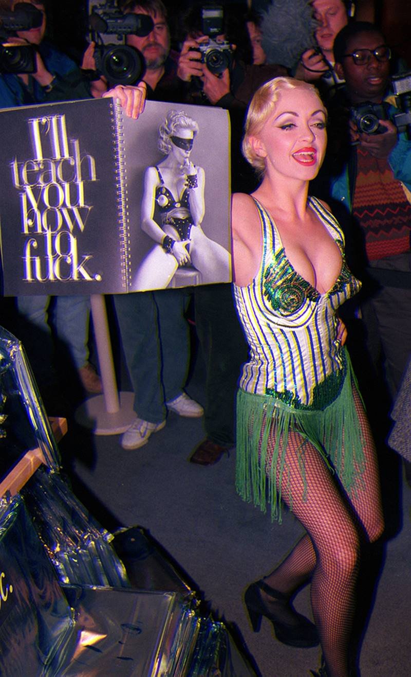 Mulher branca, jovem e loira, vestida como cover da cantora Madonna, segura uma cópia do livro Sex. A publicação da cantora foi lançada em 1992 e trazia fotos sensuais. - Metrópoles