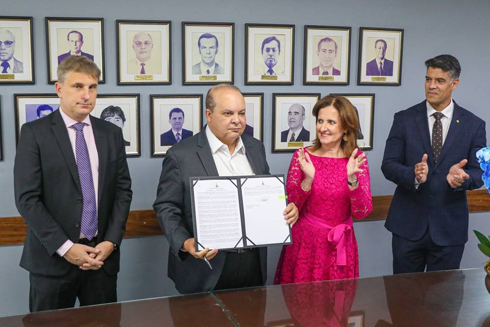 O governador Ibaneis Rocha posa para foto mostrando ato de assinatura de promoção de procuradores da PGDF. Ao lado, os procuradores aplaudem frente a uma parede com fotos dos titulares anteriores - Metrópoles