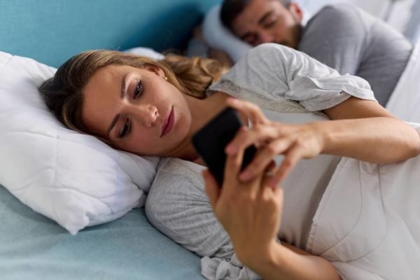 Casal deitado enquanto mulher mexe no celular e homem dorme - Metrópoles