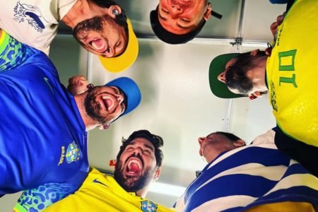 foto tirada de baixo para cima com seis homens rindo vestidos de blusas do brasil - metrópoles