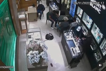 Imagem mostra quatro homens em loja. Dois de boné, um de chapéu. Assaltantes roubam joalheria