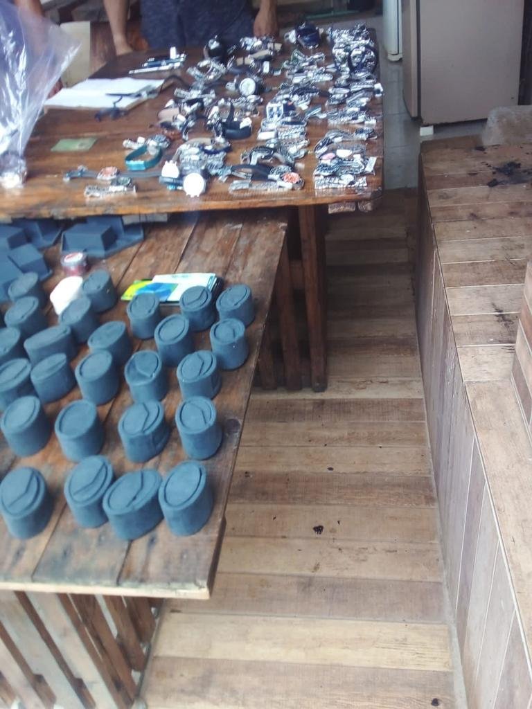 Foto mostra diversas caixas azuis de relógios e relógios de pulso sobre mesa de madeira